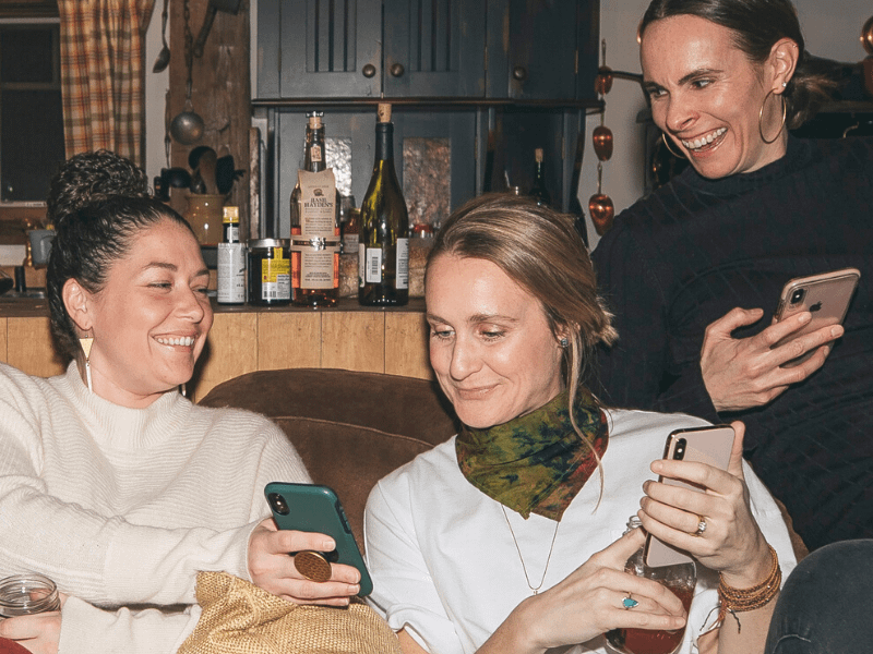 1 woman showing two other women something funny on her phone